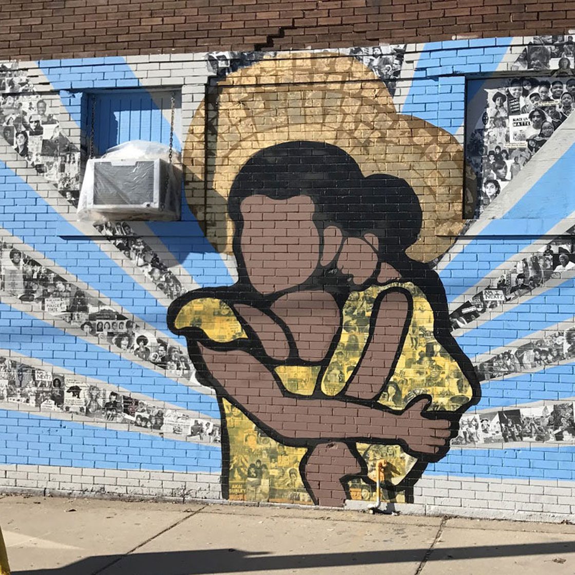 Outdoor large-scale mural of a woman holding a child with rays radiating from them