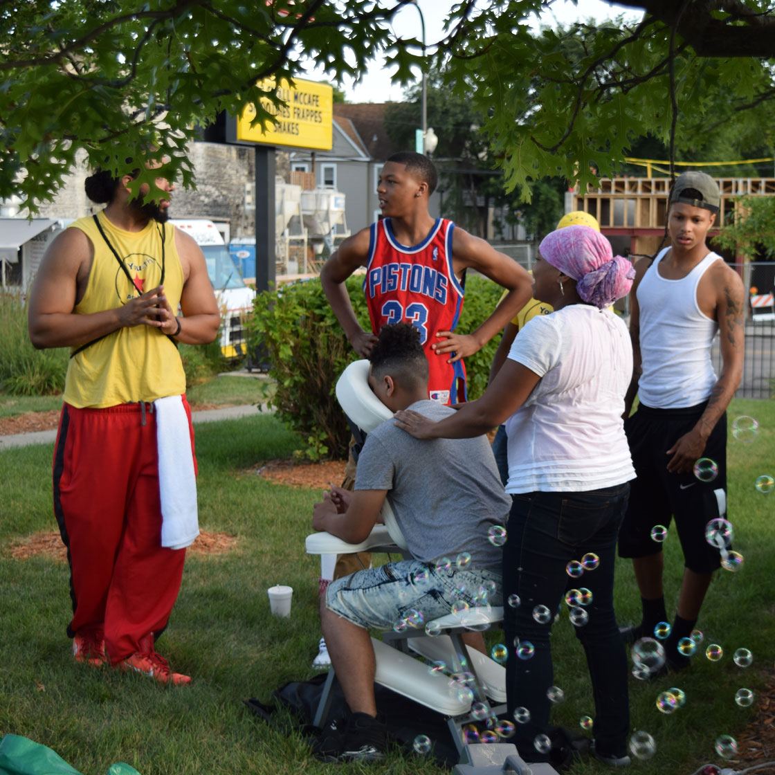 Several people milling about outside, one of them receiving a massage from another