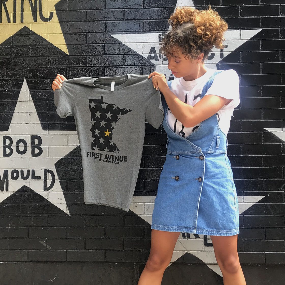 Someone holding a t-shirt up against a black wall with painted stars.