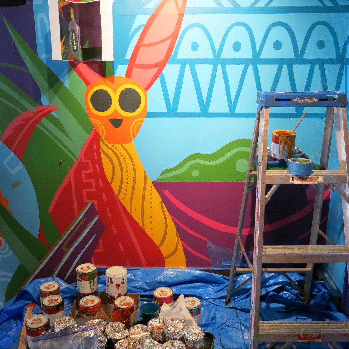 An in progress colorful graphically painted mural inside a restaurant