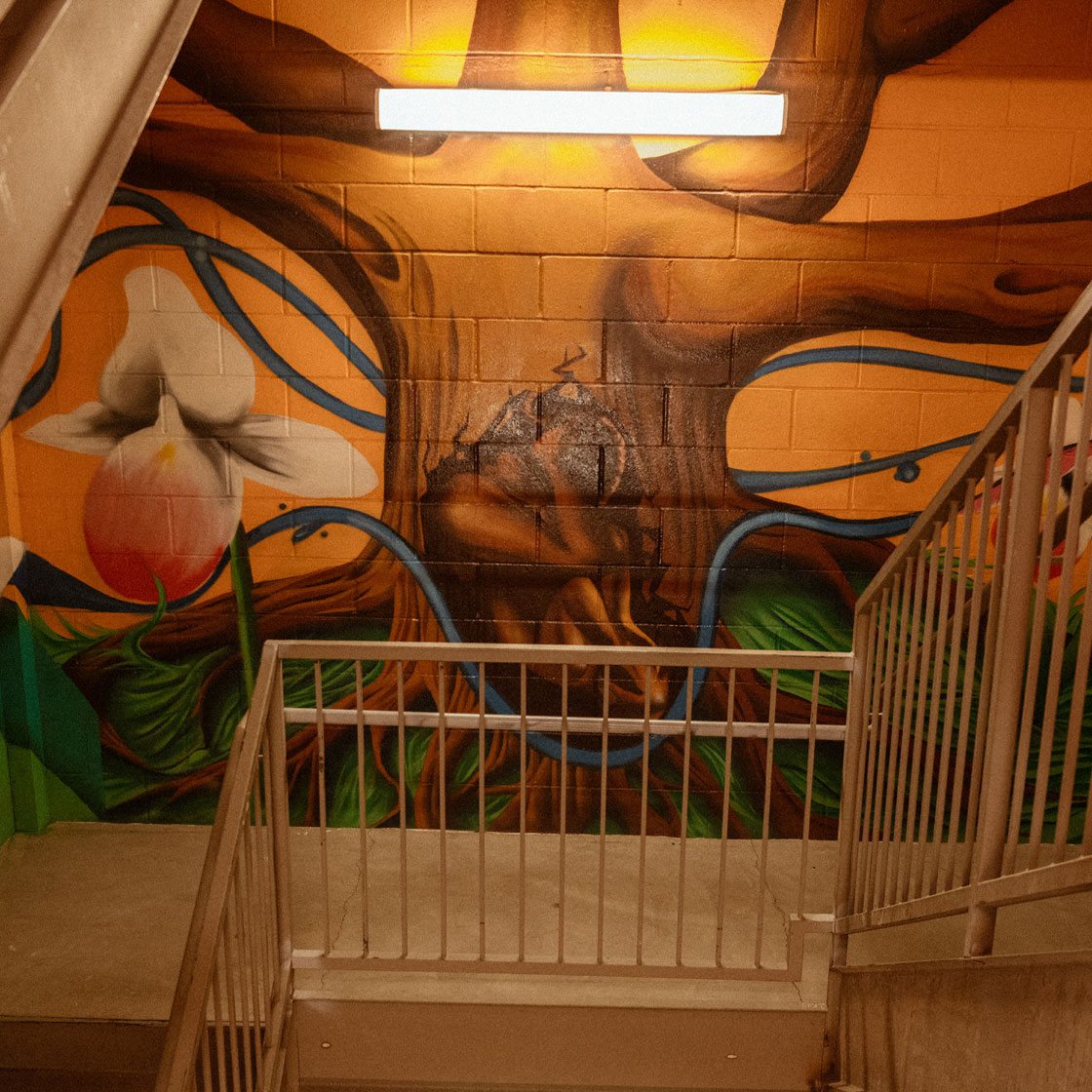 A painting in an indoor staircase of a large tree with a fetus-like figure in a womb-like position