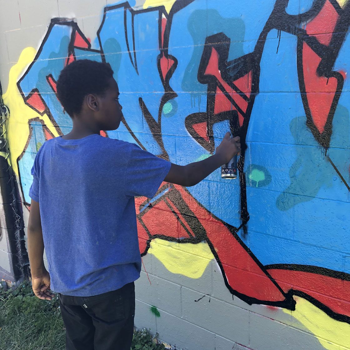A young person using a spray paint can on a colorful mural