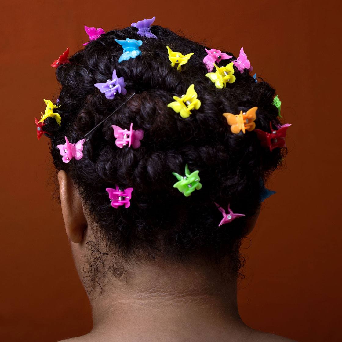 A portrait of the back of someone's head, their hair filled up with different colored butterfly clips.