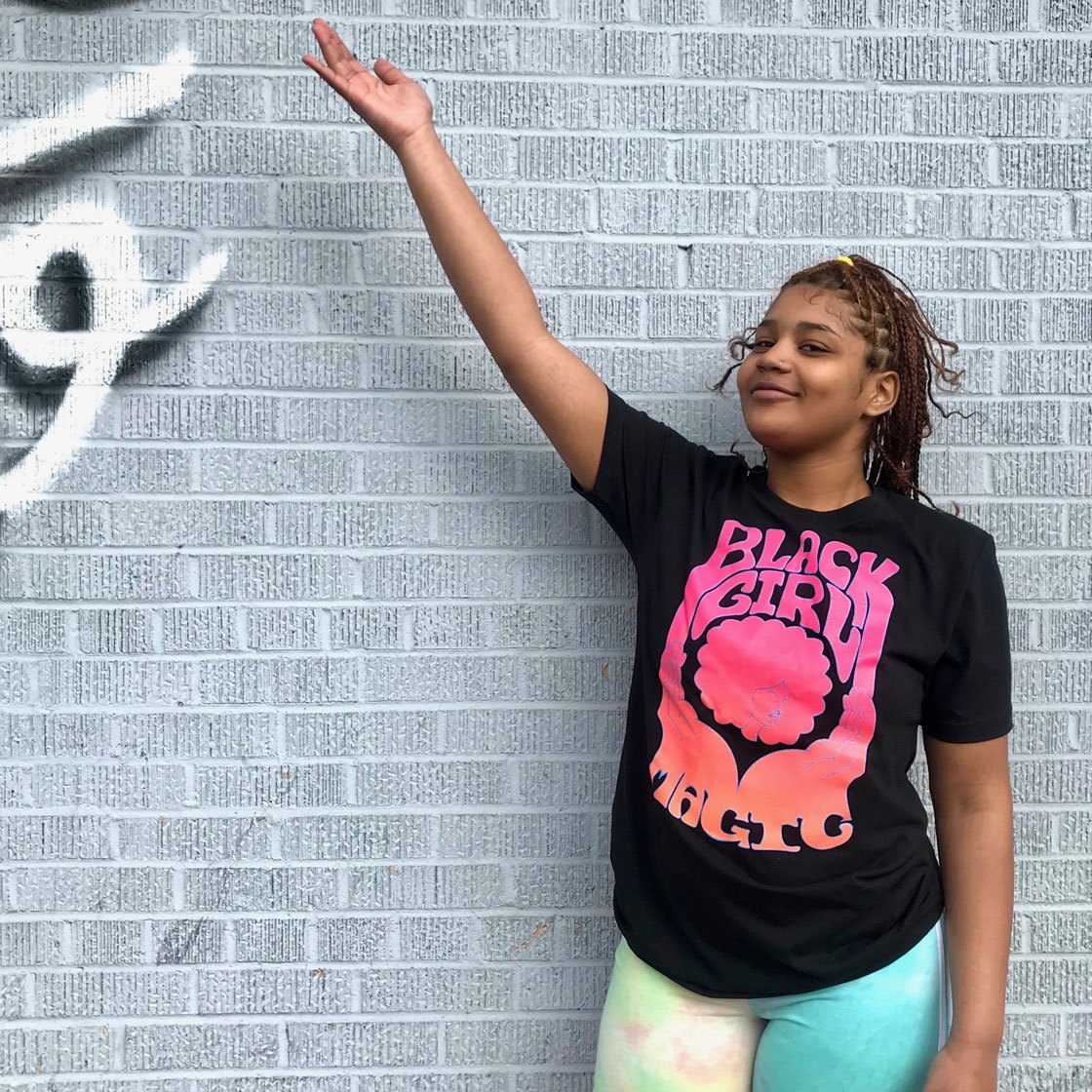 A young person posing wearing a decorative t shirt with the words black girl magic