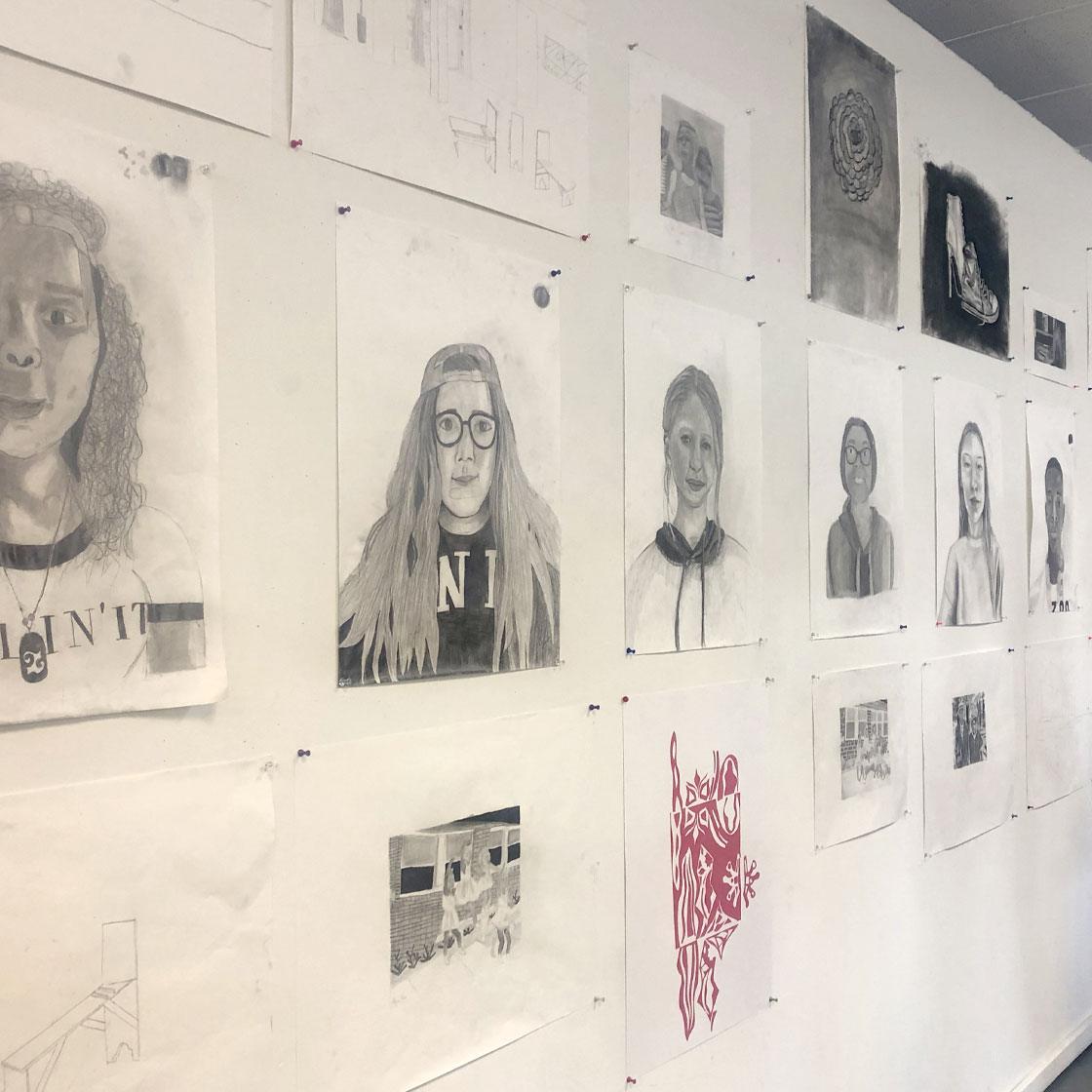 A wall displaying charcoal portrait drawings.