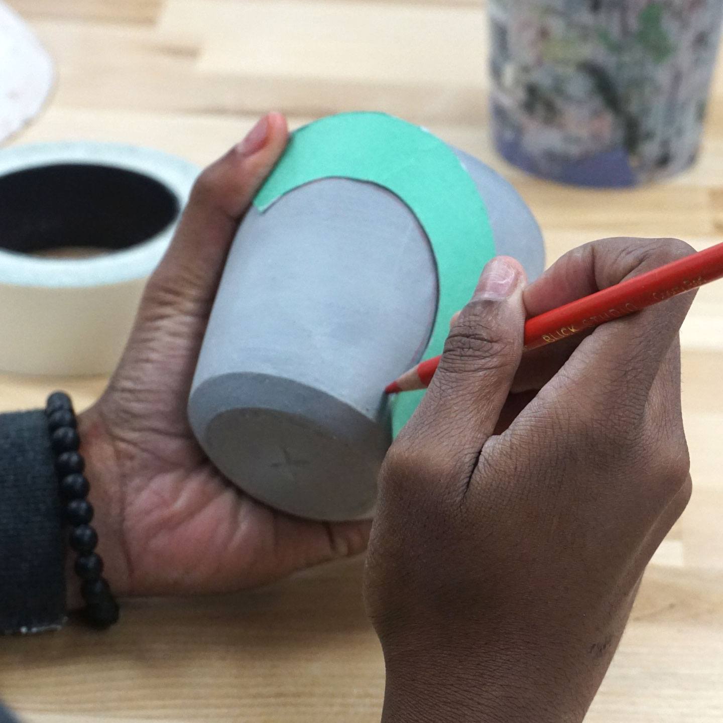 A student apprentice handling and decorating a ceramic cup.