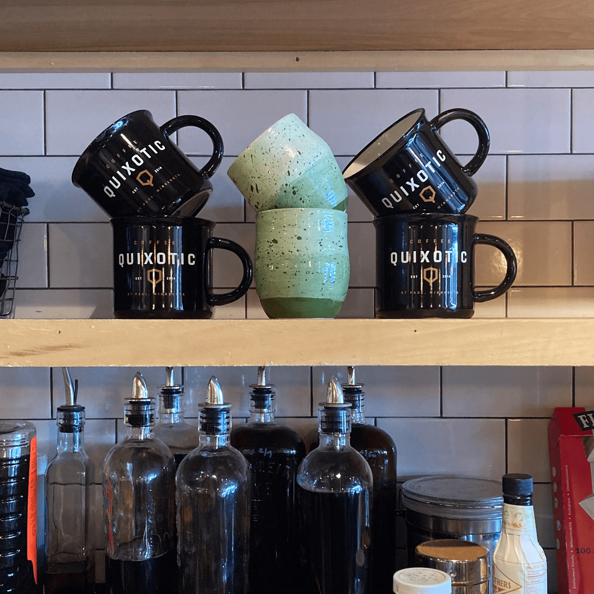 Display shelf with green ceramic mugs and Quixotic coffee mugs